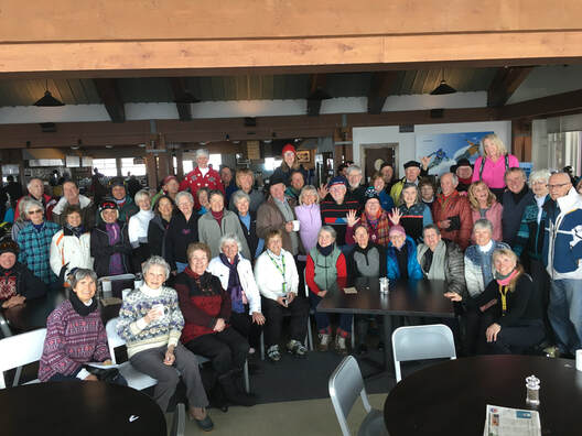 a large group of older adults pose for a photo inside the sundeck