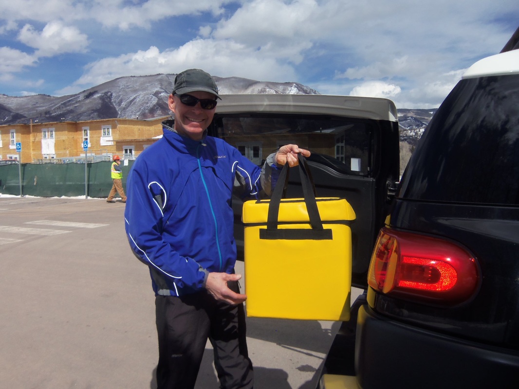 a volunteer loads an insulated bag into his vehicle with a building, mountains and cloudy blue sky in the background