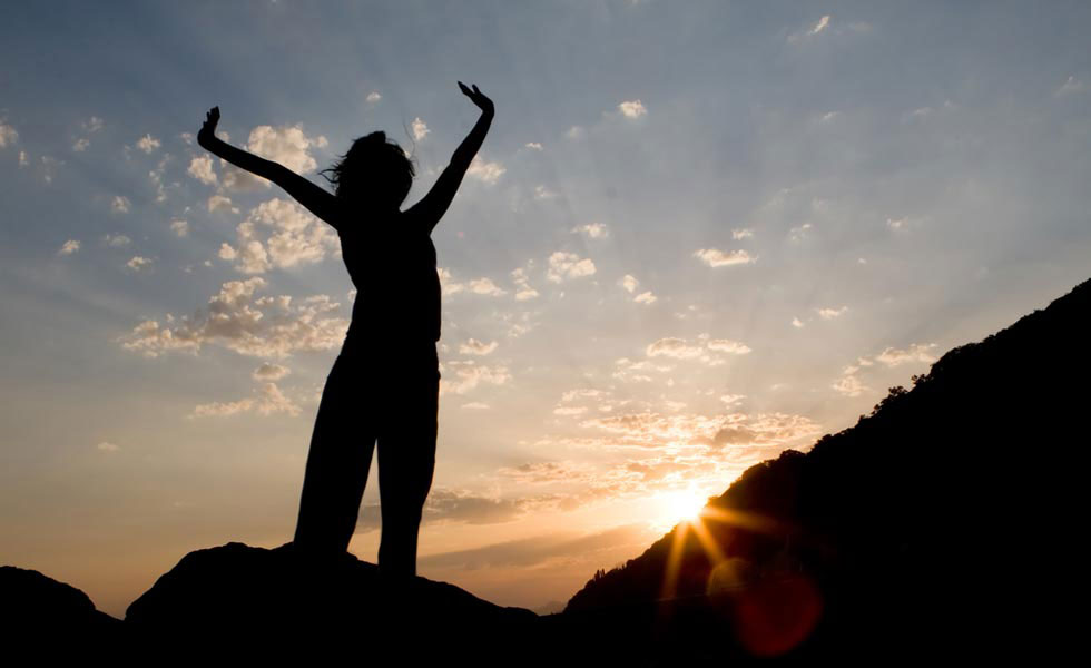 silhouette of a person stretching with mountains, sky and sun in the background